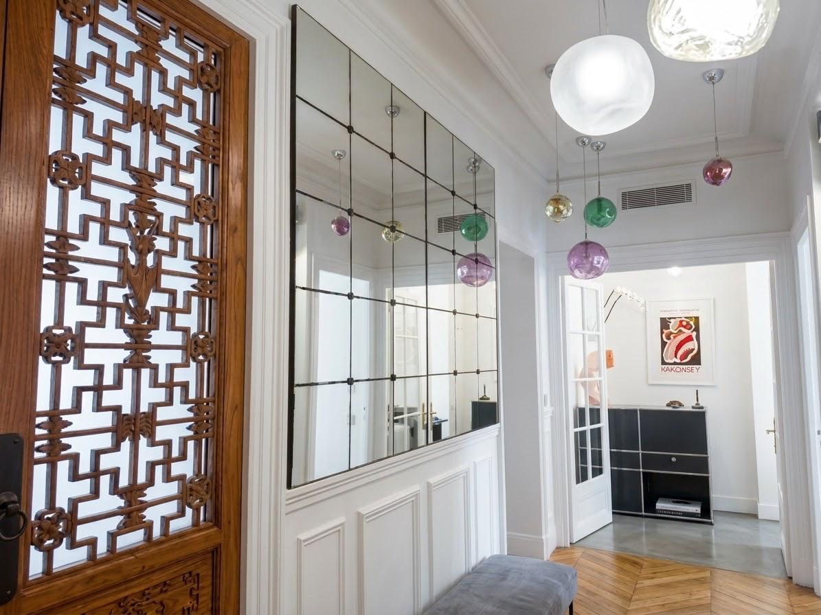 Hall d'accueil du cabinet de phlébologie du Dr Assayag-Ganem à Paris 17e : porte en bois sculpté, grand miroir et banquette d'attente